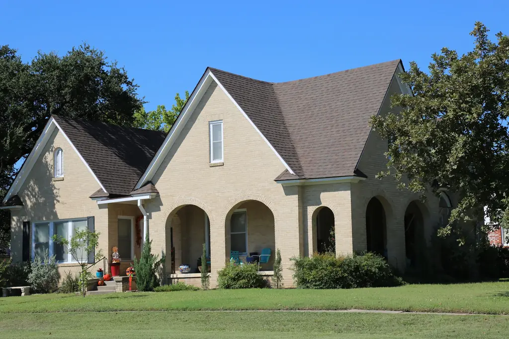 Blonde brick house with an arched porch under a new brown architectural shingle roof, fitted by Excell Roofing