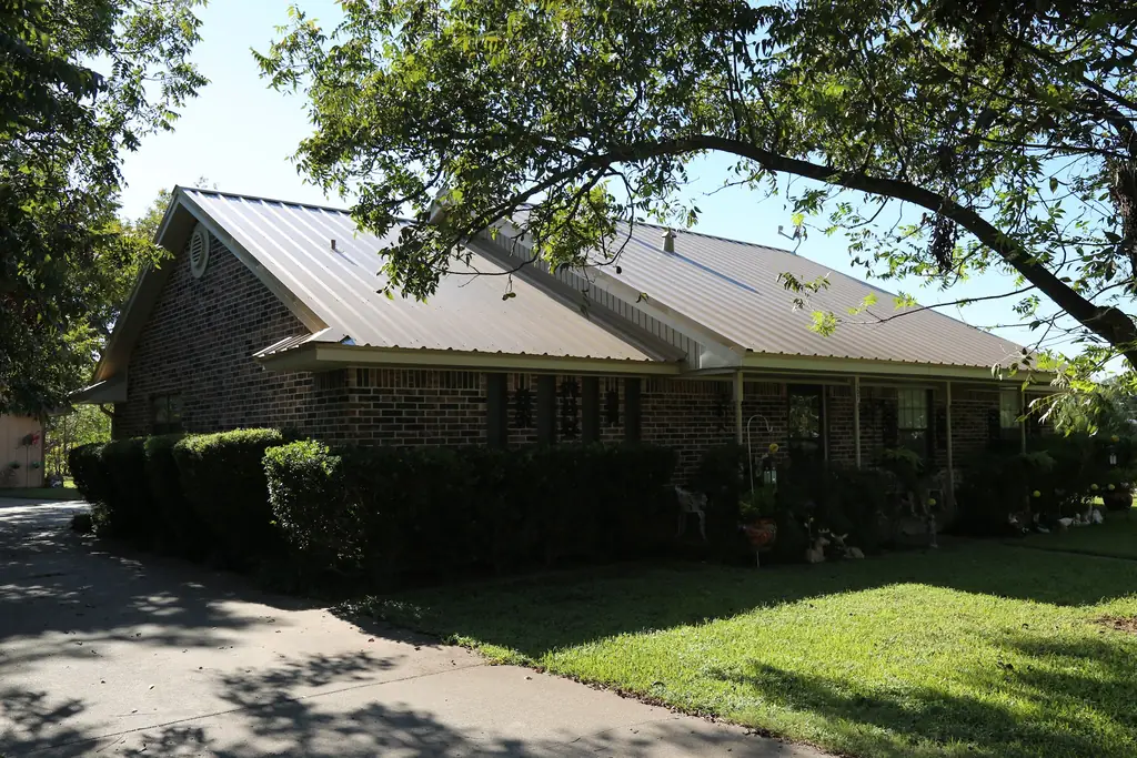 Brick ranch house with a tan R panel metal roof, framed by a pecan branch, roofed by Excell Roofing