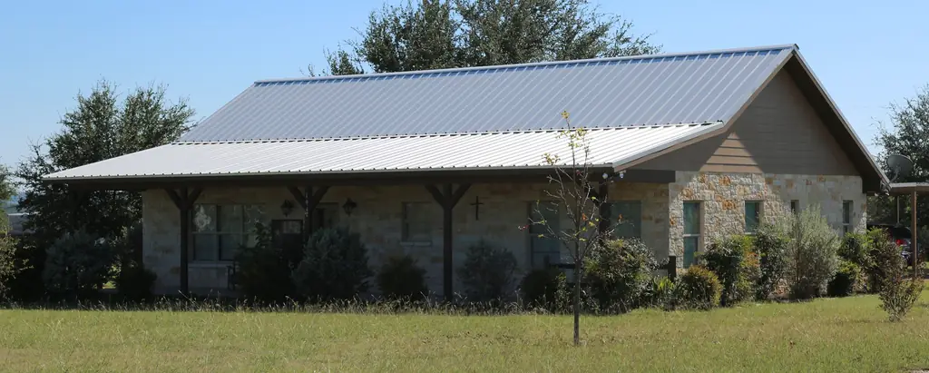 Texas limestone house with a long porch under a silver standing seam metal roof, roofed by Excell Roofing