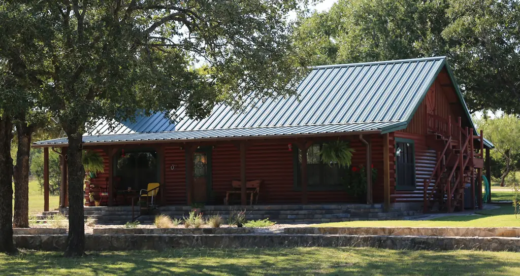 Red log cabin under a green standing seam metal roof with a covered porch, roofed by Excell Roofing